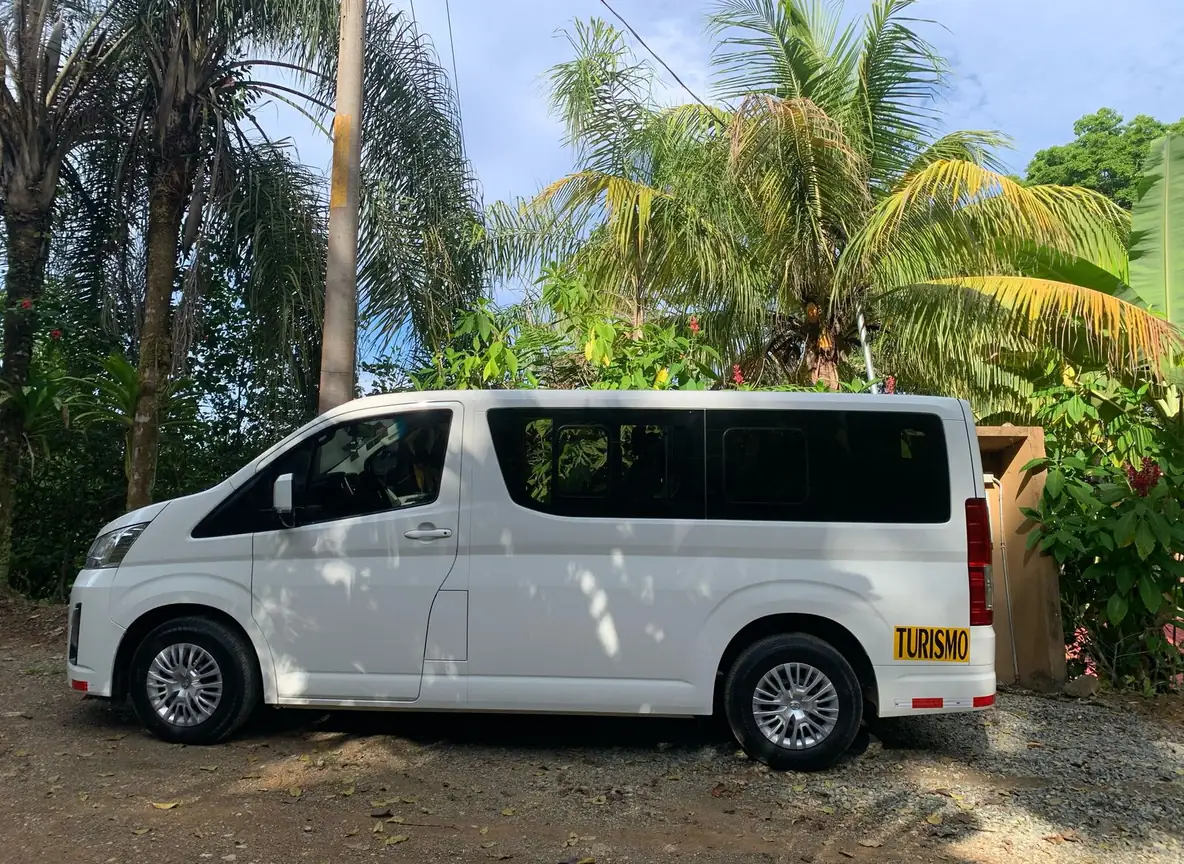 White Toyota Hiace private shuttle van with a Turismo sign, parked under palm trees in Costa Rica